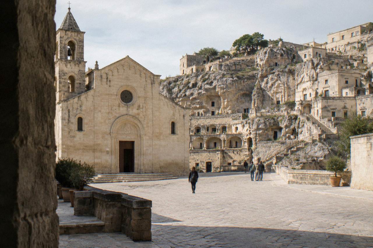 A stone square in Matera with the facade of a church and cave dwellings carved into the rock face behind it