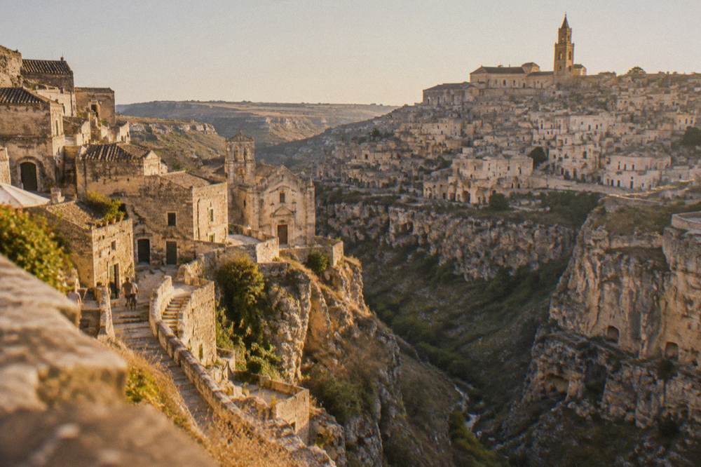 Terraced cave facades of Matera seen across a deep canyon at golden hour