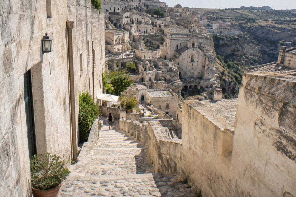 Narrow stepped lane between pale stone walls leading down into the Sassi