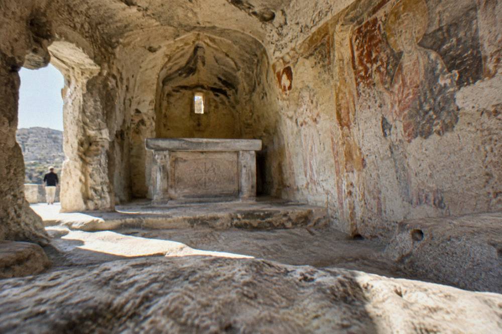 The interior of a cave church with a carved stone altar and traces of old frescoes on the rock walls