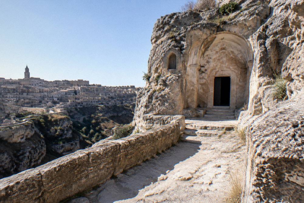 Rock church facades with small arched openings carved into a cliff face above a canyon