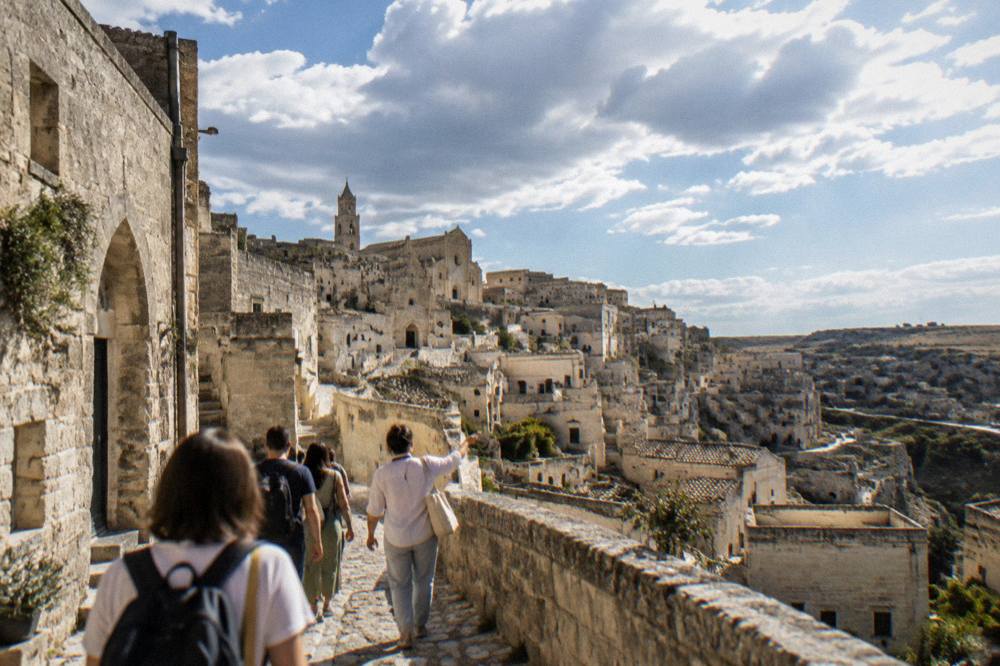 A guide leading a small group along a stone street between cave buildings in Matera