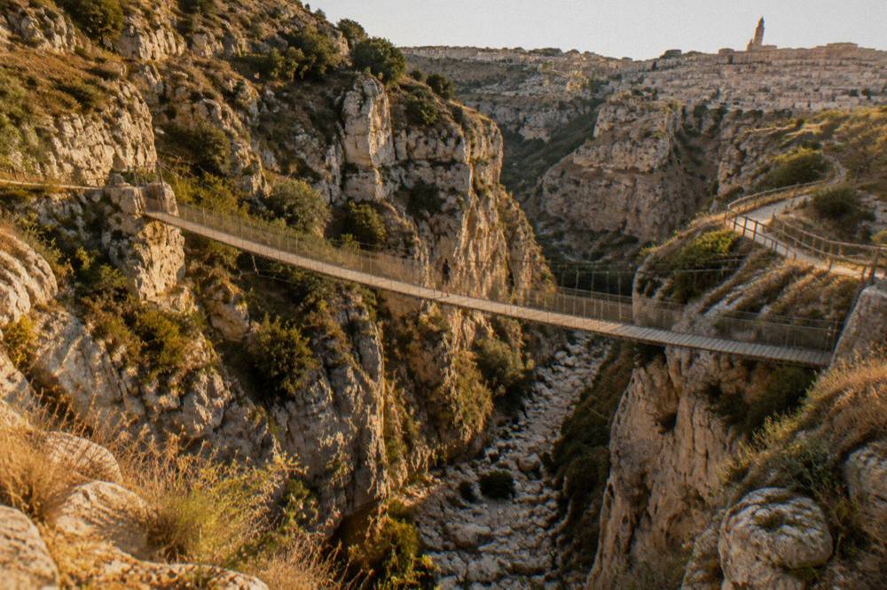 A canyon trail with a wooden footbridge over a dry streambed between limestone walls