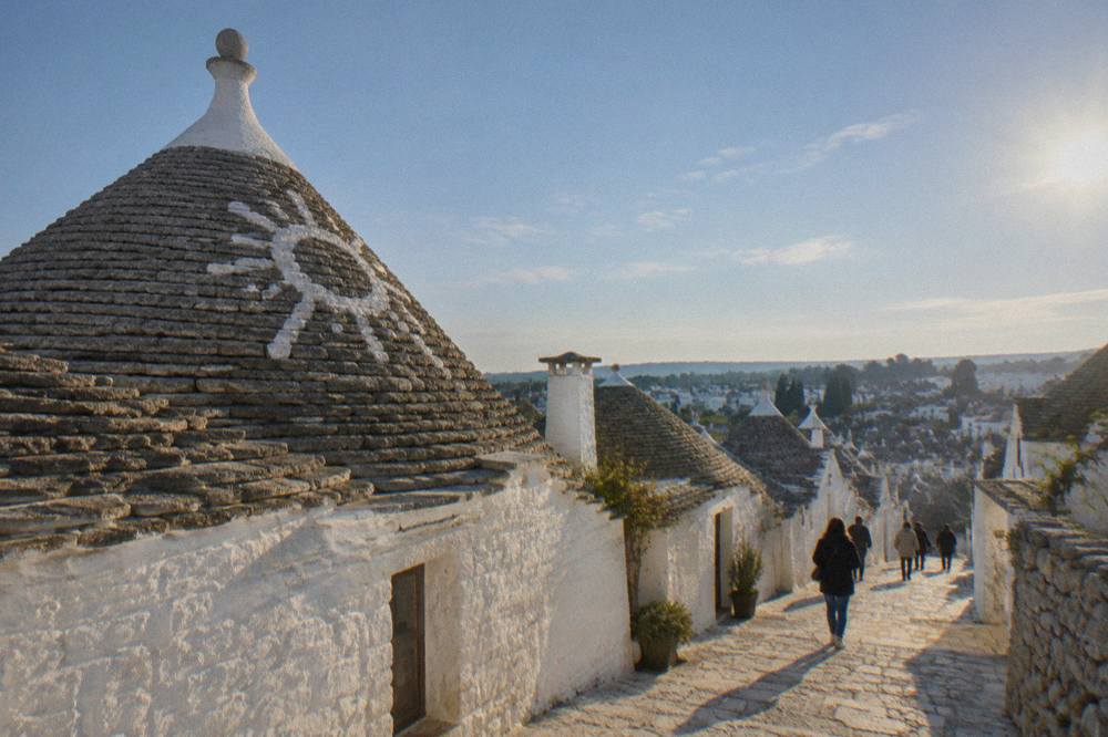 A conical trullo roof with a whitewashed stem and painted symbol seen from below
