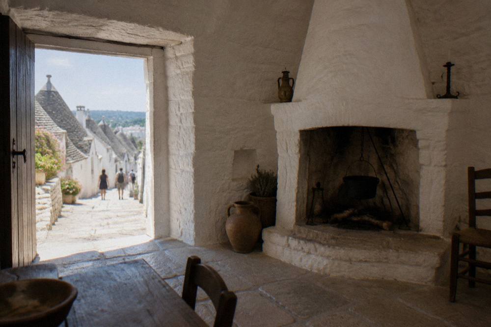 The interior of a trullo with a rounded whitewashed wall and central hearth