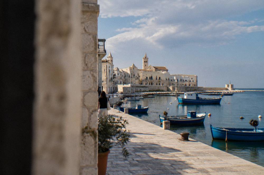 A stone seafront promenade beside calm blue water with boats moored along it