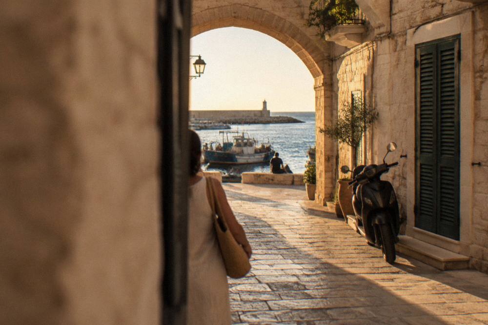 A narrow stone street in an old quarter with a scooter parked by a shuttered doorway