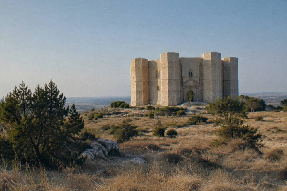 A stone castle with octagonal towers seen across open scrubland in morning light