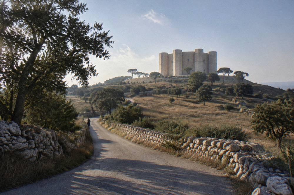 A winding country road through dry stone walls and oak scrub toward a distant castle
