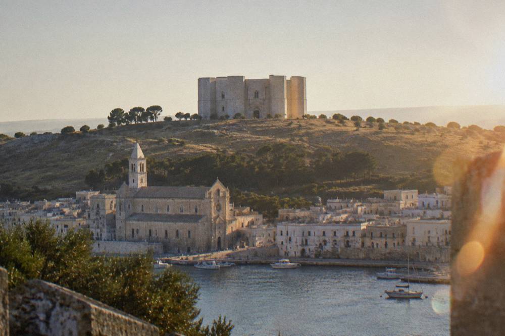 A coastal town with a stone cathedral at the water's edge seen from the harbour