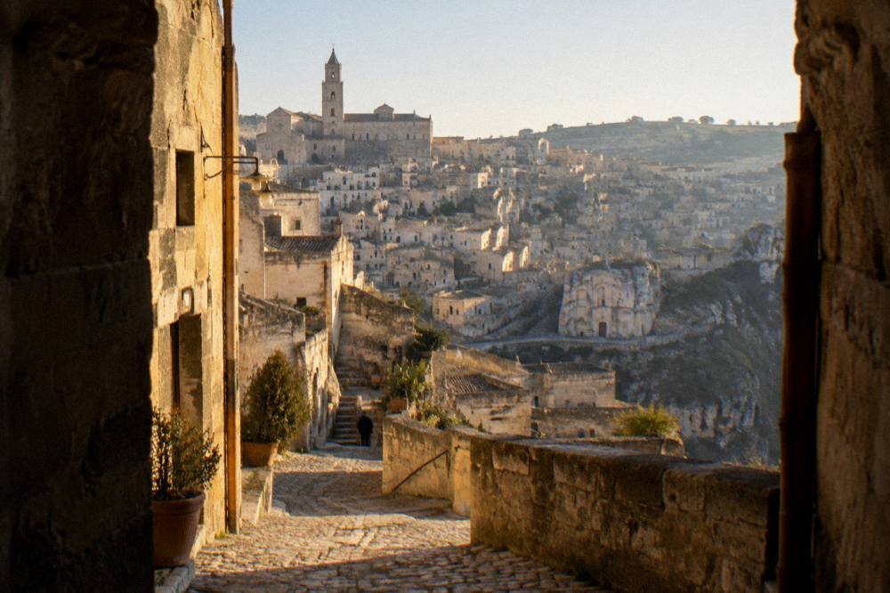 A narrow cave street in Matera lit warmly at dusk with stone facades