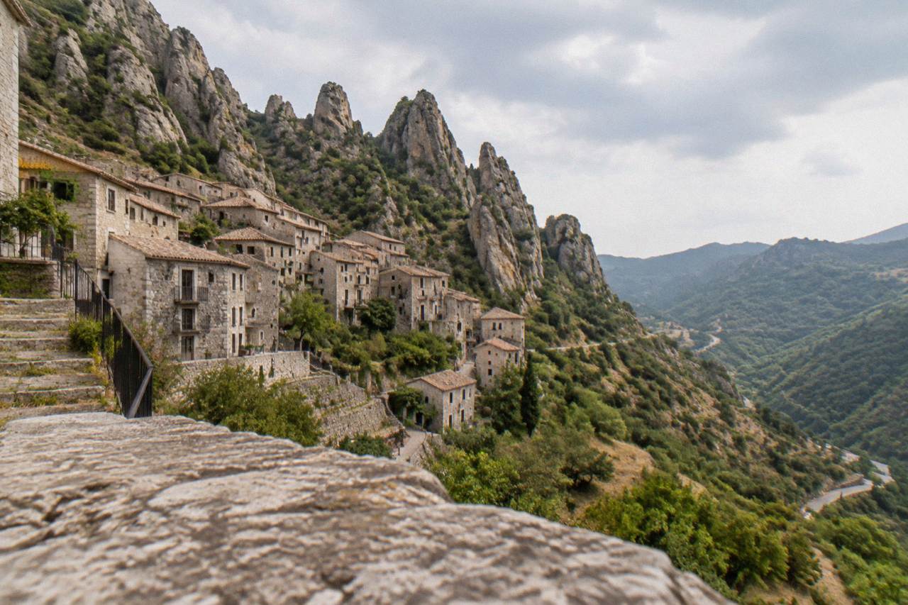 Stone village houses stacked on a steep green mountainside below a rocky ridge