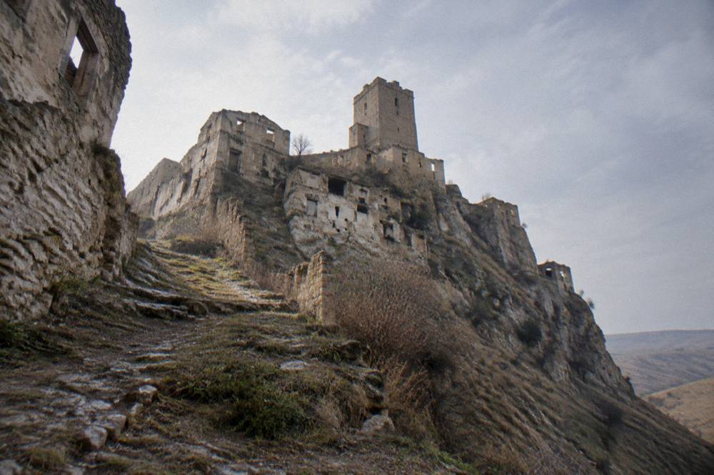 A stone watchtower and cluster of ruined buildings on a hill crest seen across a valley of erosion gullies