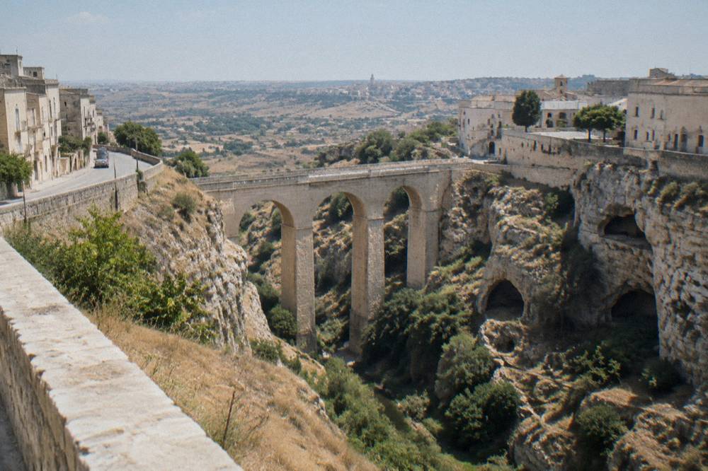 A plateau road crossing the southern Italian countryside toward a distant town