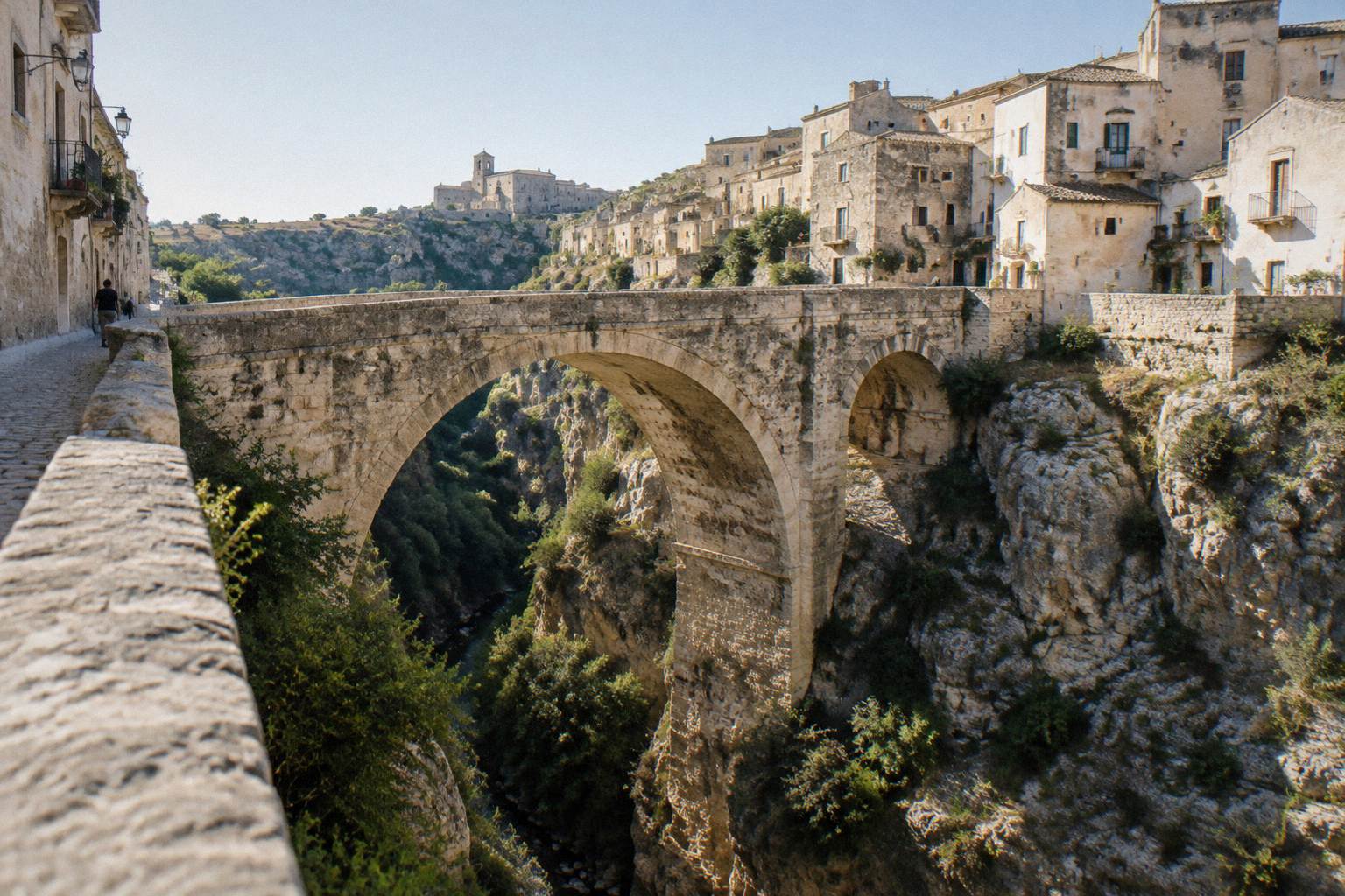 Stone arched bridge crossing a deep limestone ravine beside old houses
