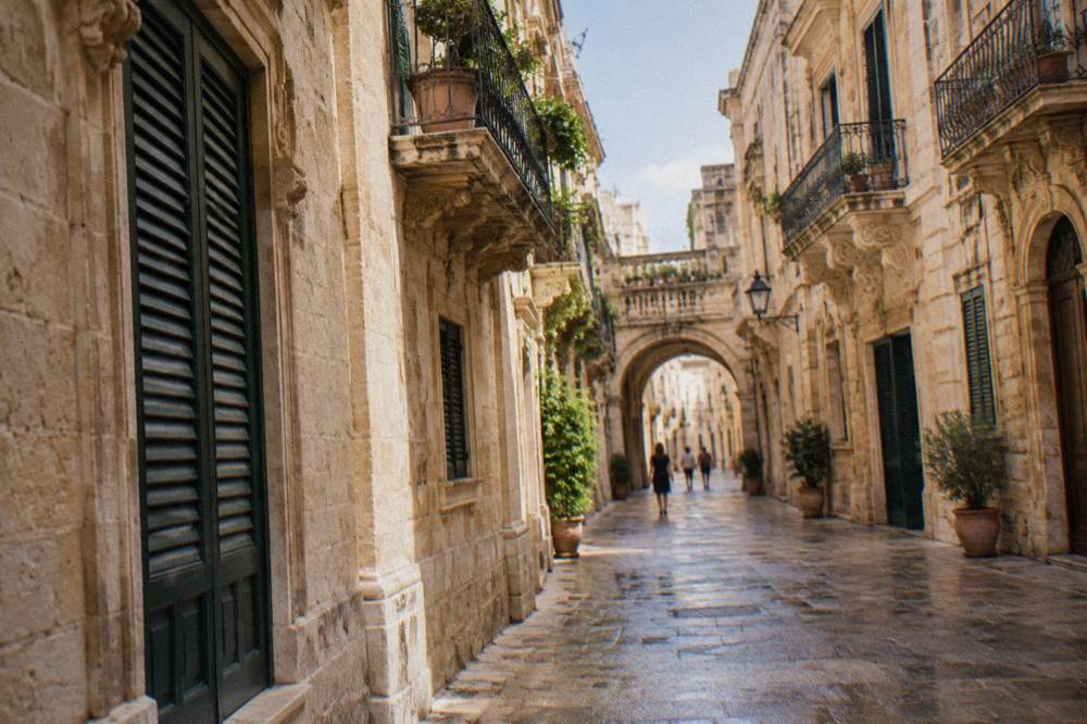 A quiet lane in Lecce's old centre with stone arches and shuttered windows