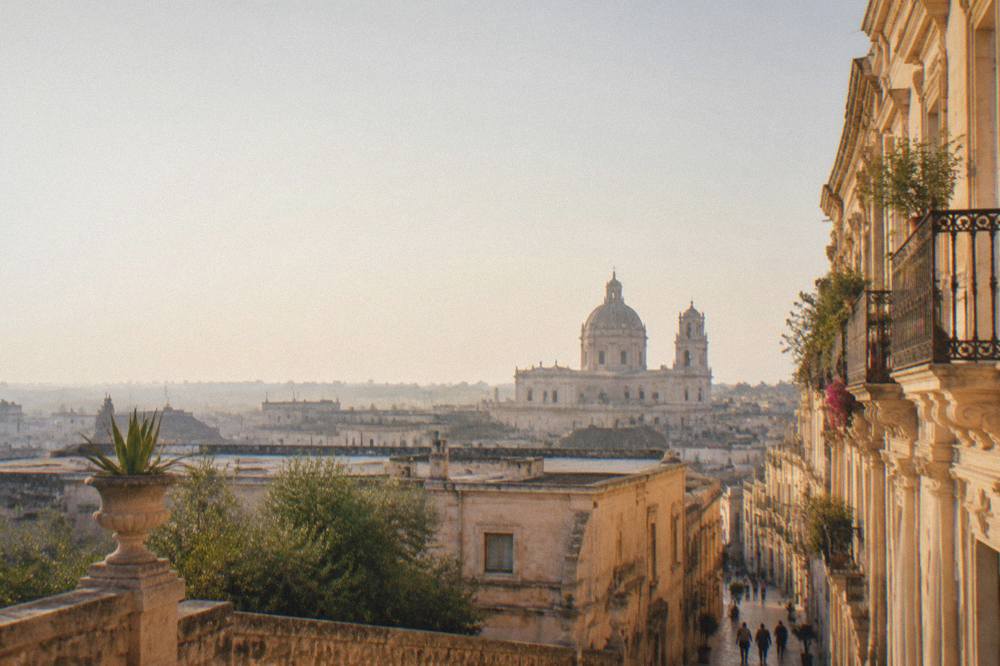 A view over pale stone rooftops toward a baroque church dome at dusk