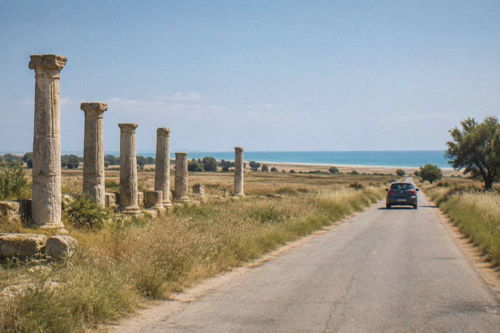 A car travelling a straight country road through flat farmland toward the sea
