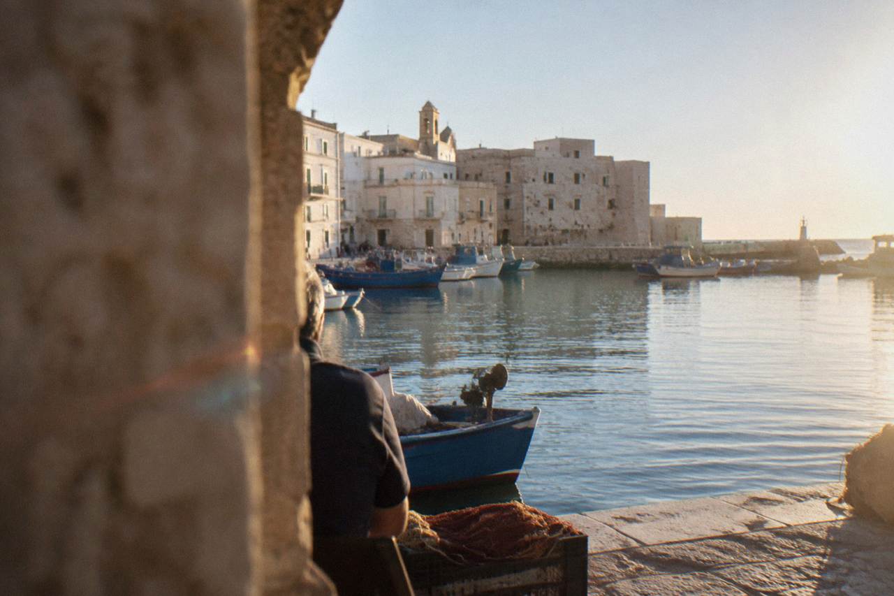 Monopoli's old harbour with fishing boats moored beside pale stone walls under a clear sky