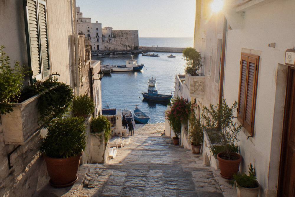 A narrow whitewashed street in Monopoli's old town with wooden shutters and potted plants