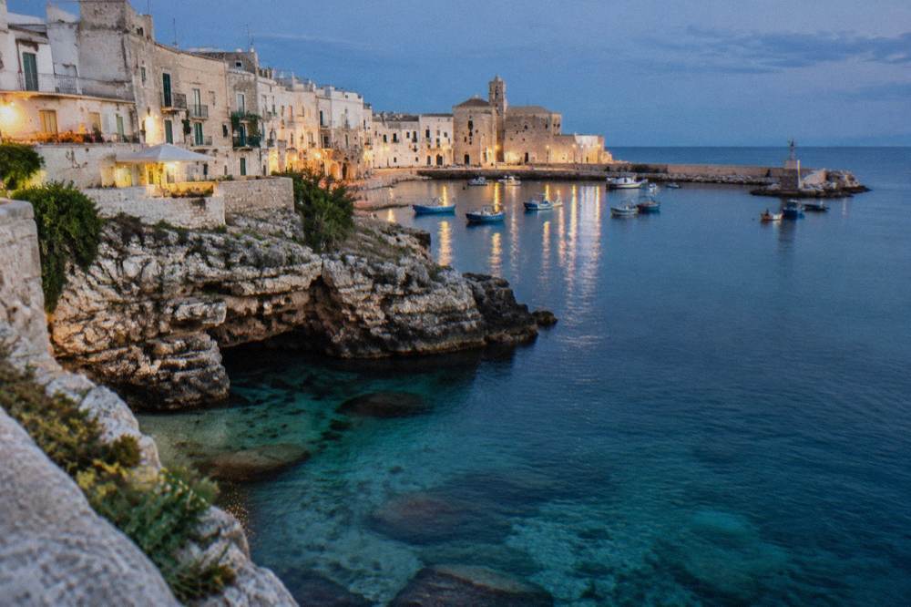 A rocky cove with clear turquoise water below Monopoli's sea walls