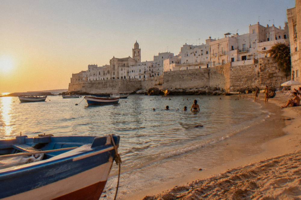 Fishing boats and swimmers sharing a small sandy beach below Monopoli's walls