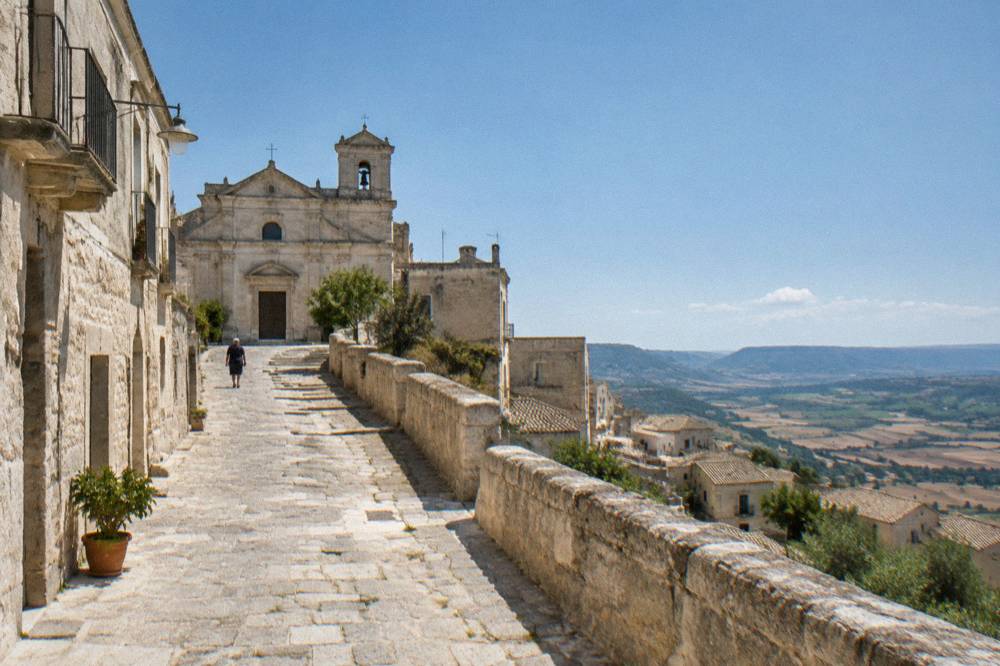 A narrow stone street climbing towards a church facade in a small Italian hilltown