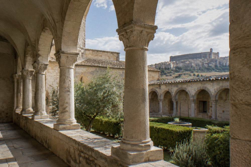 The cloister of an old Italian abbey with stone arches and afternoon light