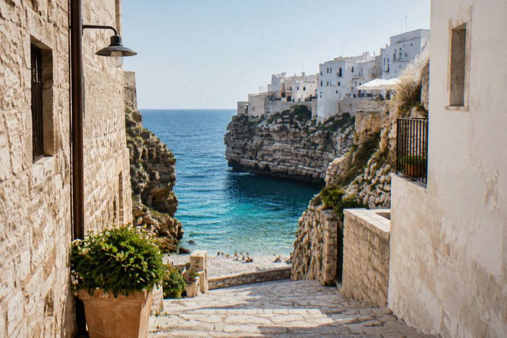 A narrow stone street in a cliffside town leading toward bright open water