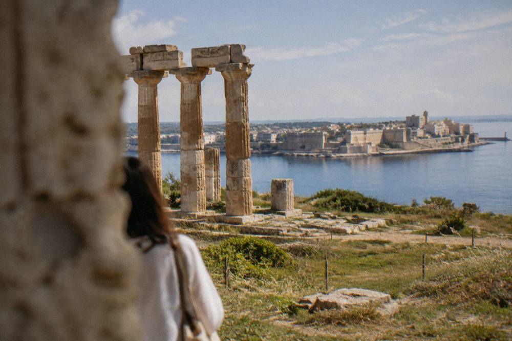Ancient stone columns of a Greek temple standing in a field near the coast