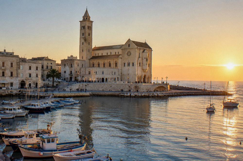 The pale stone facade of Trani cathedral seen from the harbour at sunset
