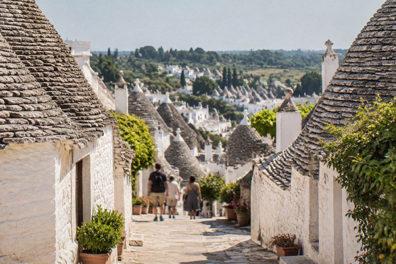 Rolling green countryside with a cluster of whitewashed houses and trulli cones in the distance