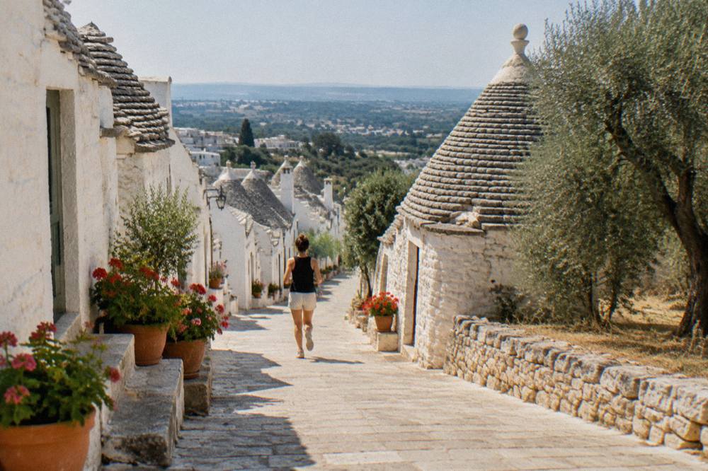 A dry-stone trullo with a conical roof standing among olive trees under a clear sky