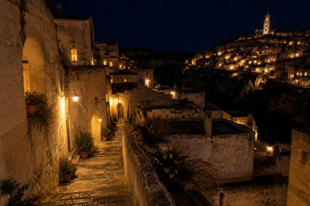 Stone stairway between pale cave buildings in the Sassi lit by warm lamps at night