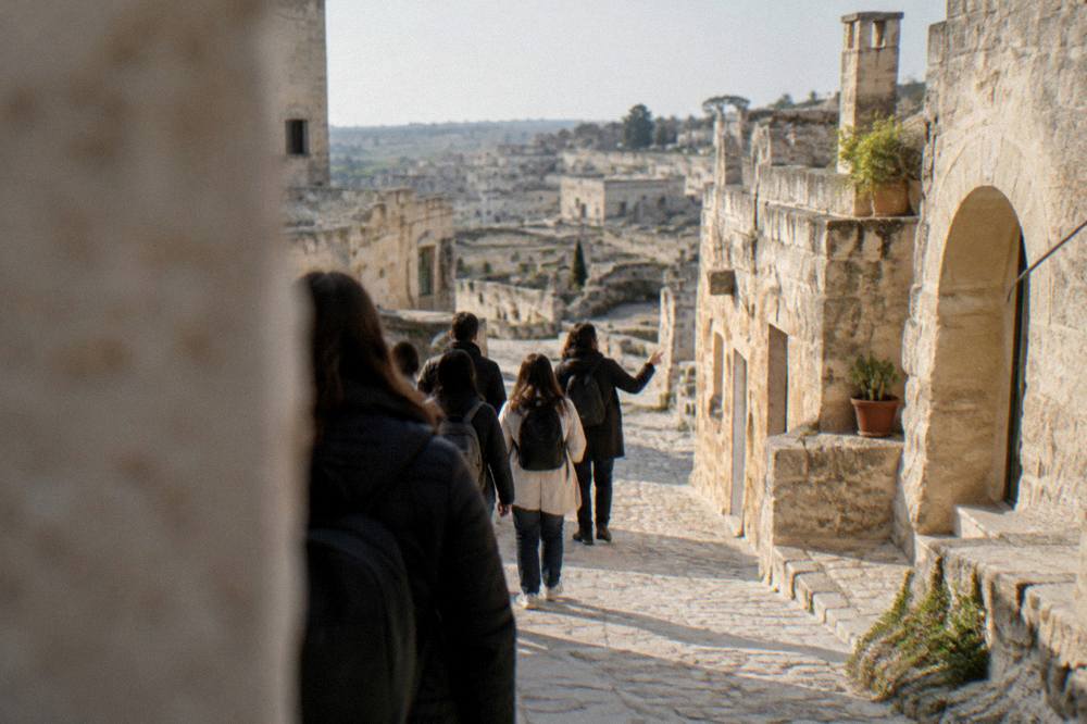 A group of visitors walking with a guide through a narrow stone lane between cave dwellings