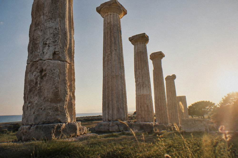 Ancient Greek temple columns standing in a field near a coastal plain at golden hour