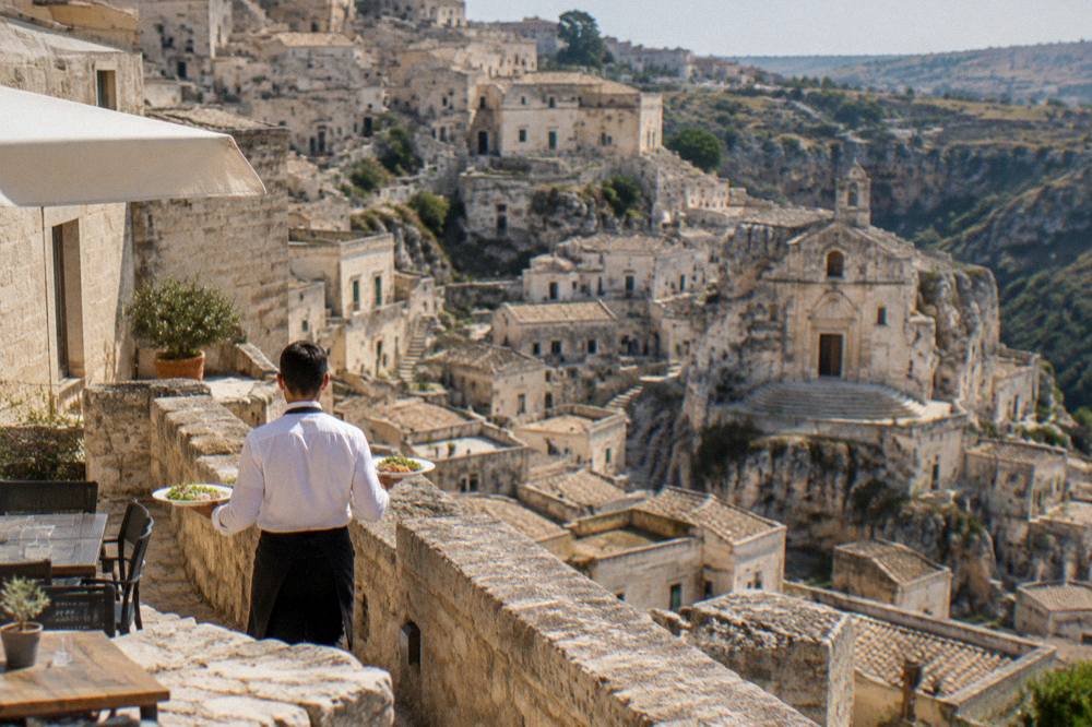 A waiter carrying plates to a stone terrace above the Sassi of Matera