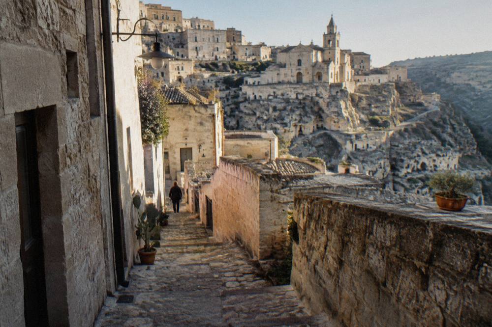 A narrow stepped alley between stone houses in Matera in late afternoon shade