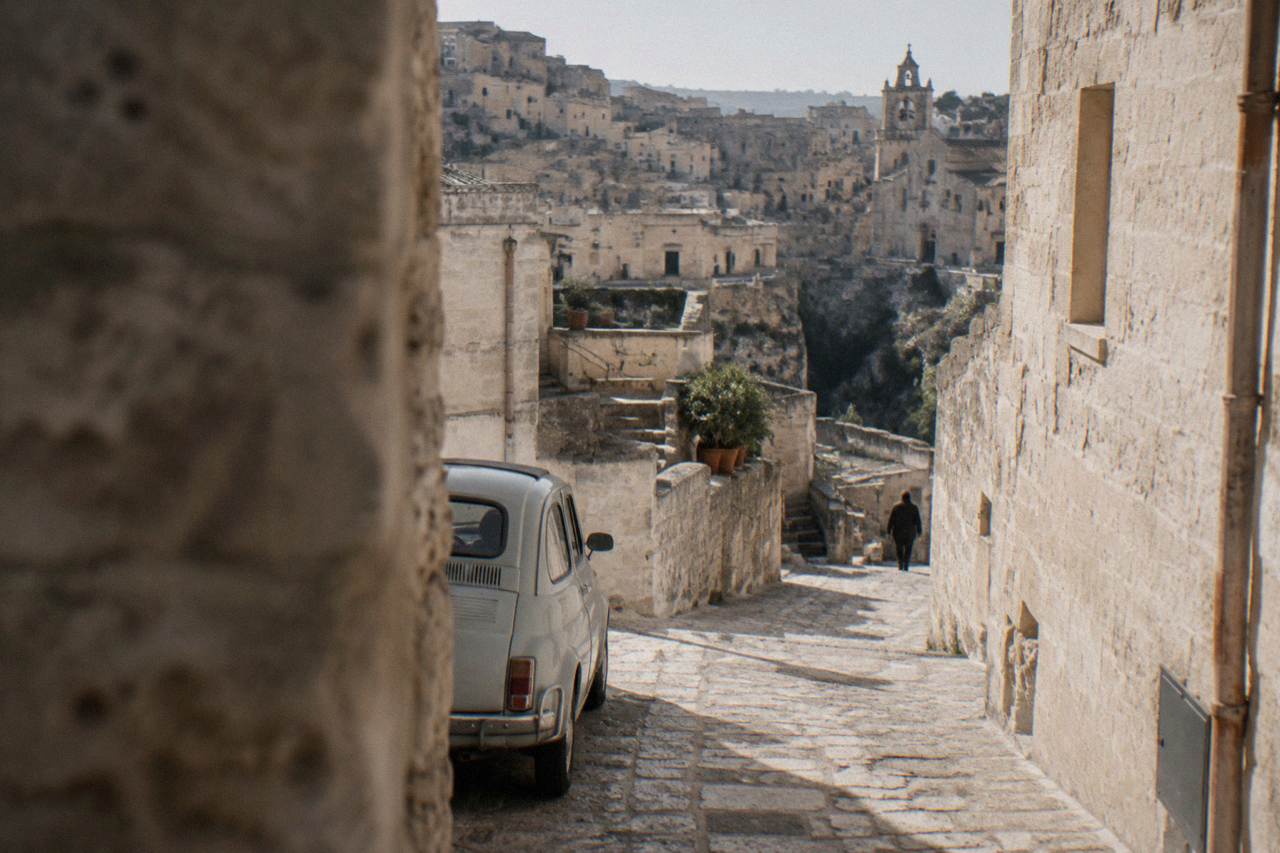 A narrow stone street in the Sassi of Matera with a small car parked beside pale tufa walls