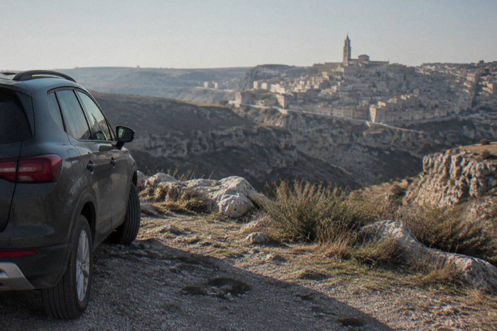 A car parked at a viewpoint overlooking the Sassi of Matera across the Gravina canyon