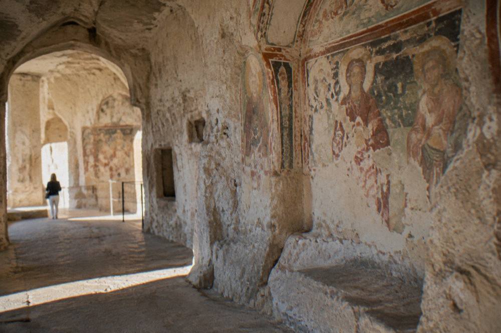 A rock-cut church interior with frescoes carved into pale stone