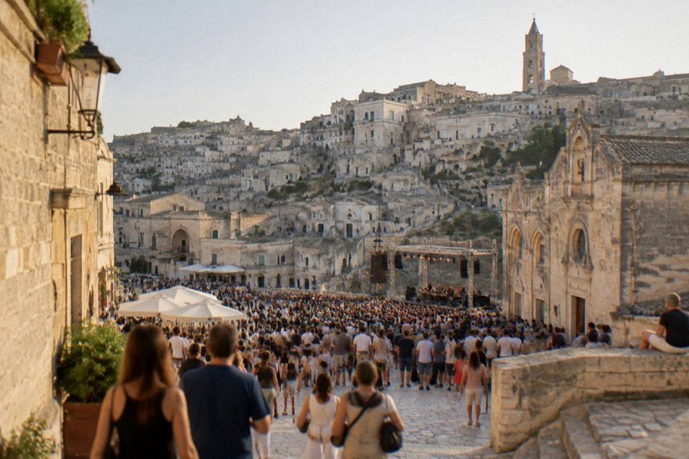 Crowds filling a stone square in Matera during a summer festival evening