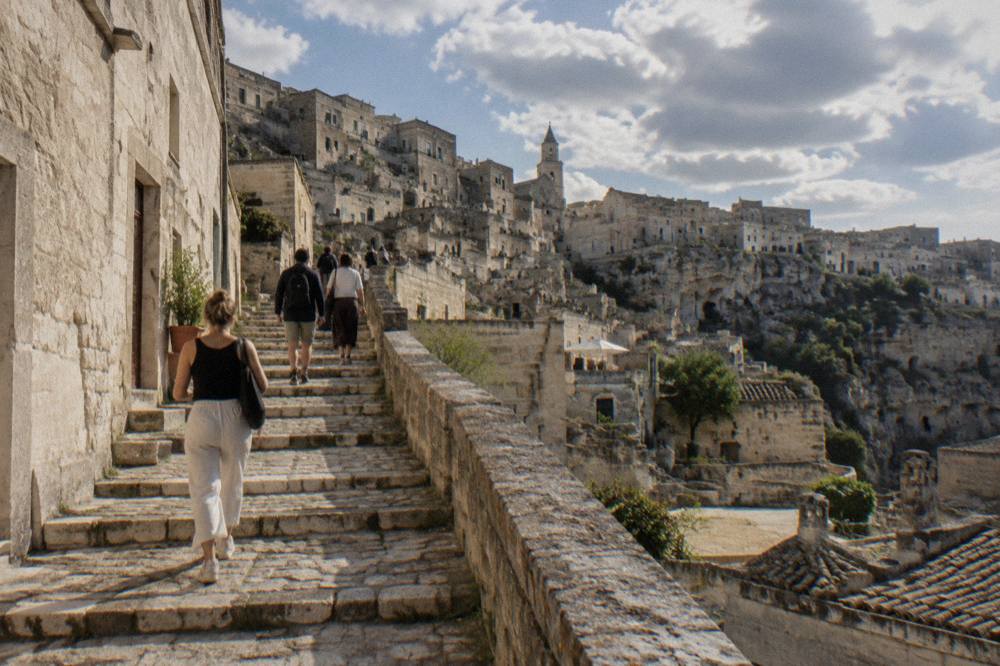 Pedestrians walking up a stone staircase street in the Sassi district of Matera