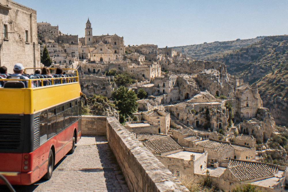 An open-top sightseeing bus parked on a street above the Sassi rooftops in Matera