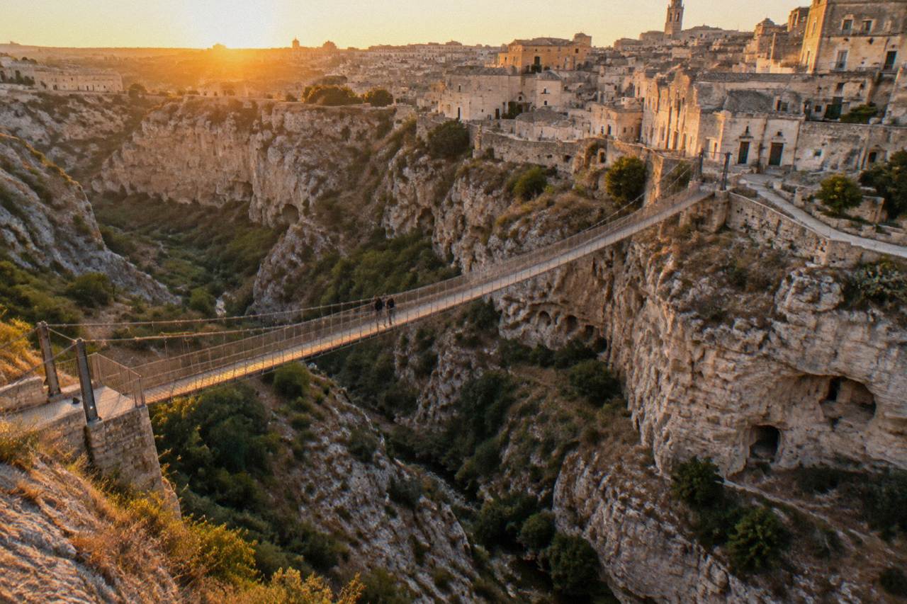 A pale limestone canyon with cave openings in its cliffs below a stone city at dusk