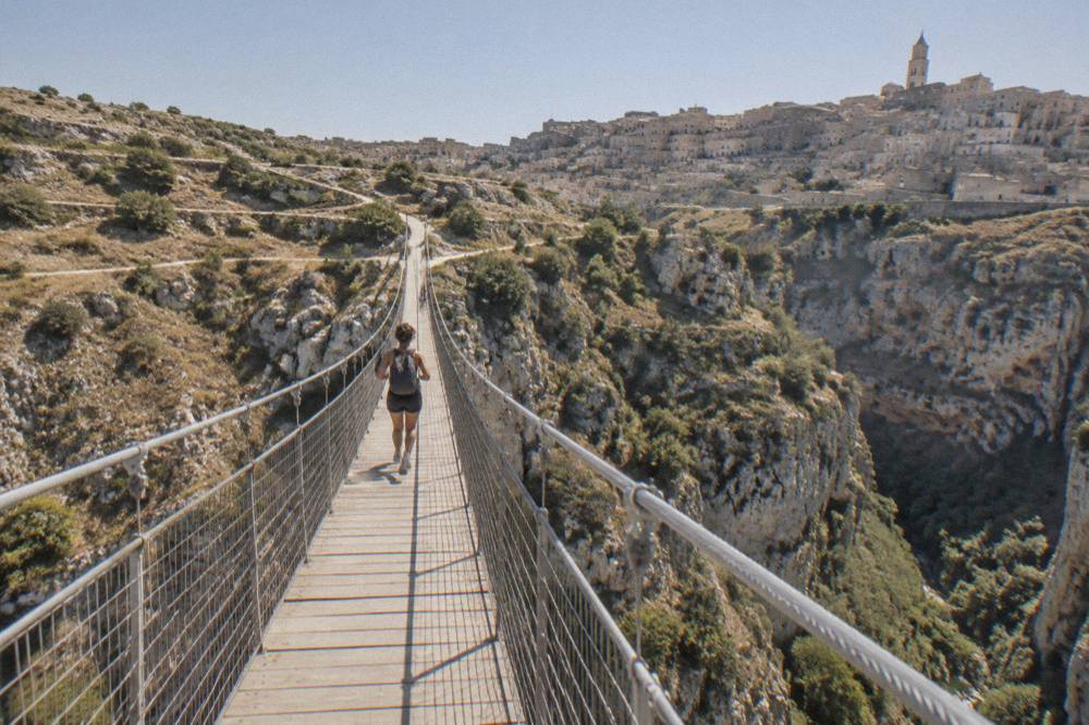 A narrow footpath winding through dry scrub on a limestone plateau toward a distant stone city