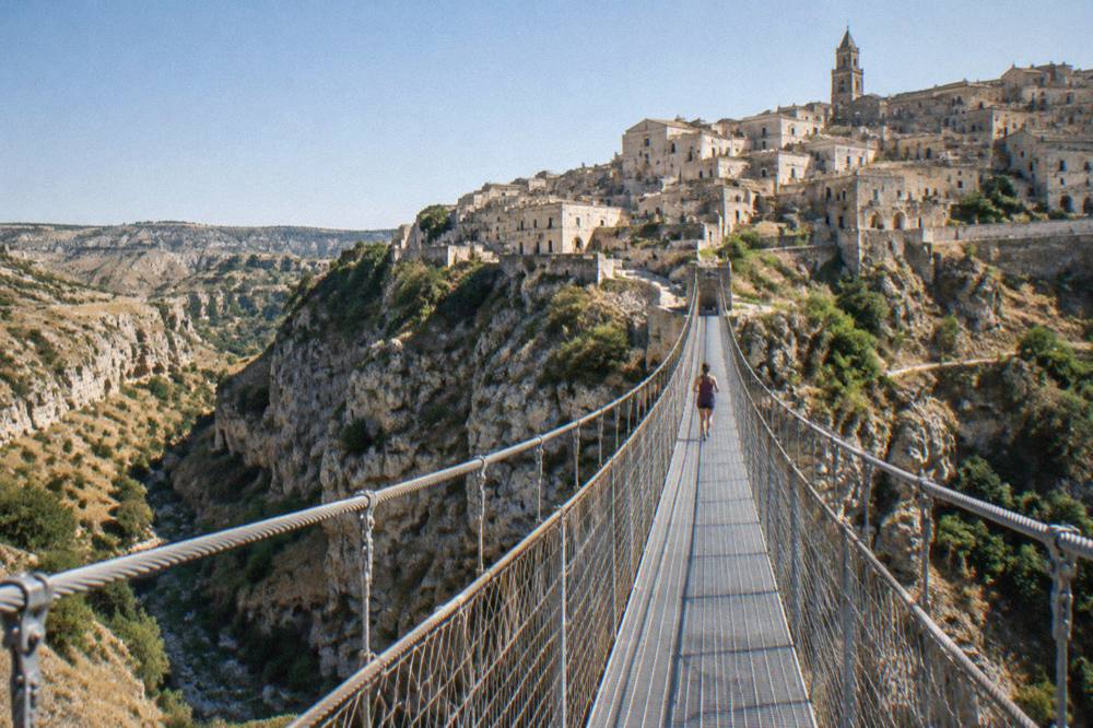 An abandoned stone hill town on a narrow ridge above eroded clay badlands under a clear sky