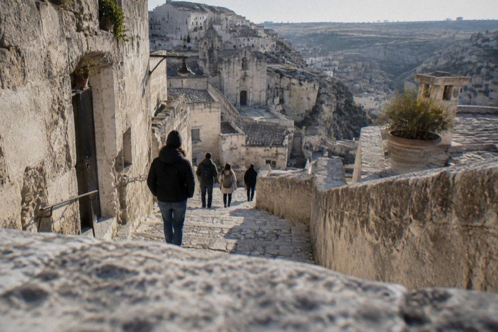 Travellers walking down a narrow stepped lane between stone houses in the Sassi