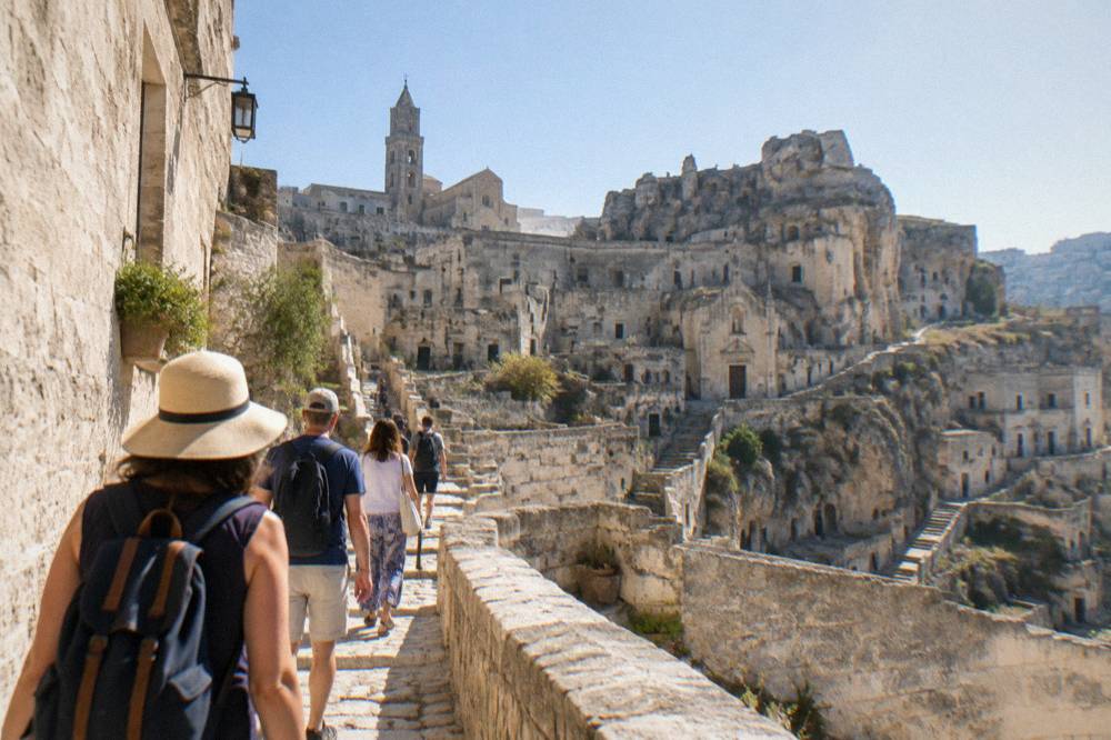A guided group of visitors walking through a sunlit lane in the Sassi districts of Matera