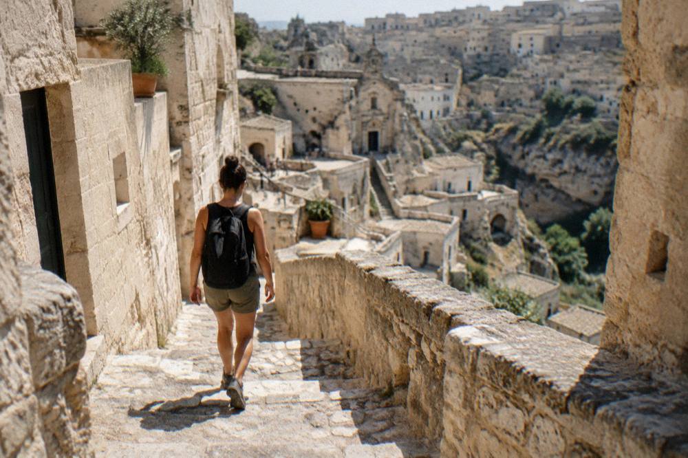 A visitor in sturdy walking shoes descending a worn stone staircase between cave buildings in Matera